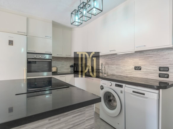 Modern white kitchen with black countertops and a stacked fridge, oven, and microwave built into cabinets.