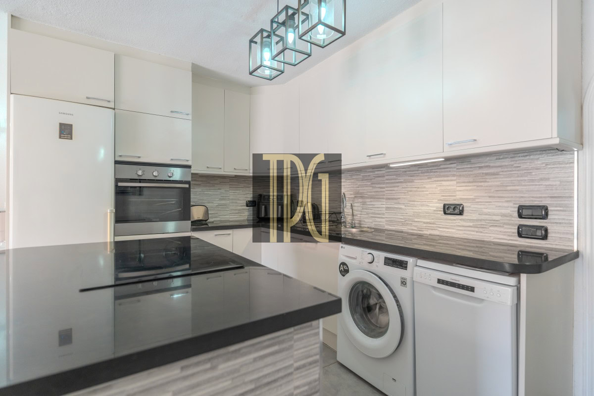 Modern white kitchen with black countertops and a stacked fridge, oven, and microwave built into cabinets.