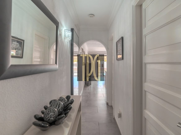 Bright hallway with white walls, a large mirror on the left, decorative stones on a shelf, and an arched doorway ahead.