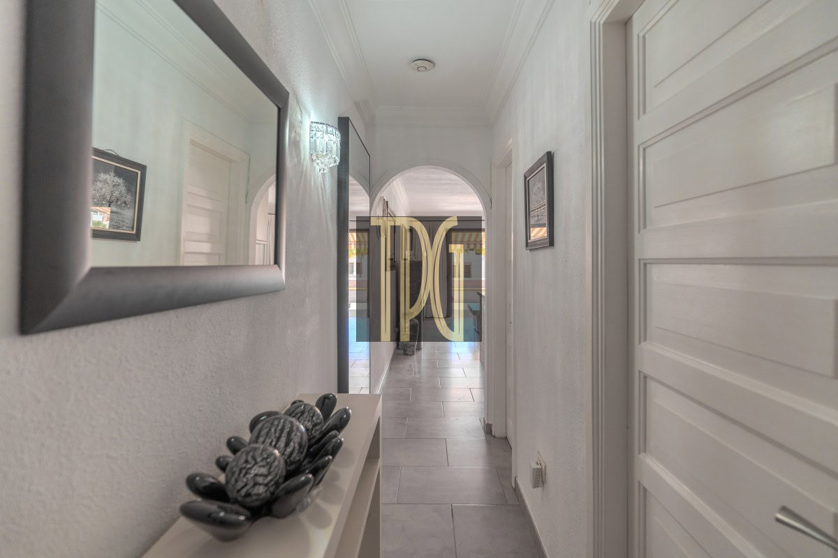 Bright hallway with white walls, a large mirror on the left, decorative stones on a shelf, and an arched doorway ahead.