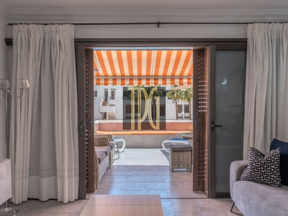 Living room opens to a sunlit terrace with an orange-striped awning, wicker chairs, and outdoor seating.
