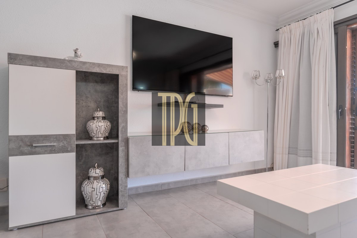 Modern living room with a wall-mounted TV above a light gray storage unit and floating shelves; decorative lantern vases on a gray cabinet.