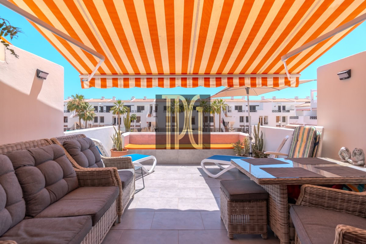 Rooftop patio with an orange-and-white striped awning, wicker couches, and a glass-topped dining table.