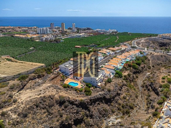 Aerial view of hillside homes along a cliff by the ocean, with a blue swimming pool and winding streets.