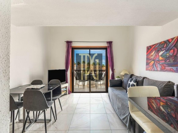 Living room with a gray sofa, abstract right wall art, and a glass sliding door opening to a balcony with purple curtains.