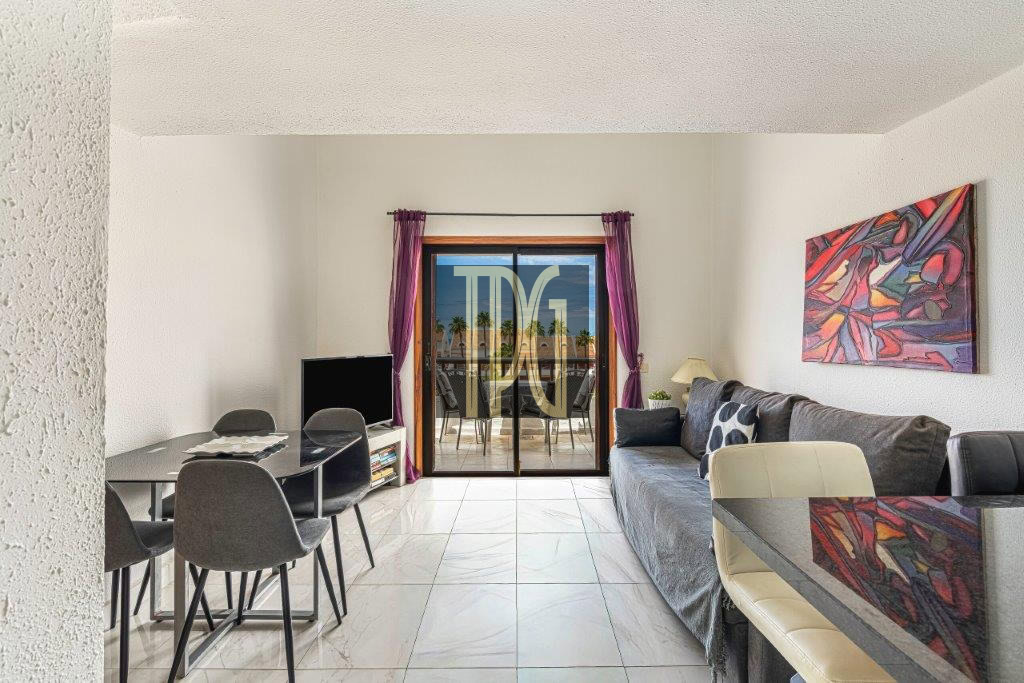 Living room with a gray sofa, abstract right wall art, and a glass sliding door opening to a balcony with purple curtains.