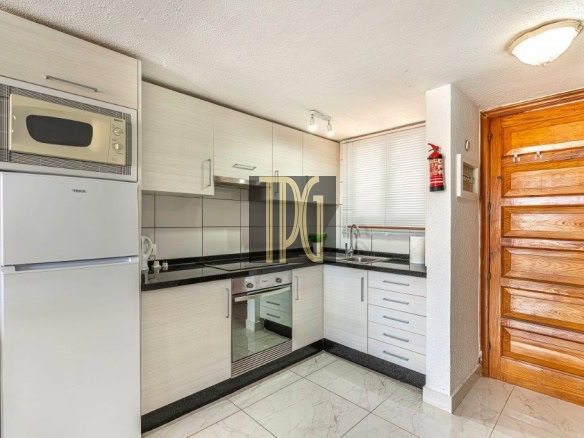 Modern L-shaped kitchen with white cabinets, black countertops, and built-in oven/microwave; wooden entry door on the right.