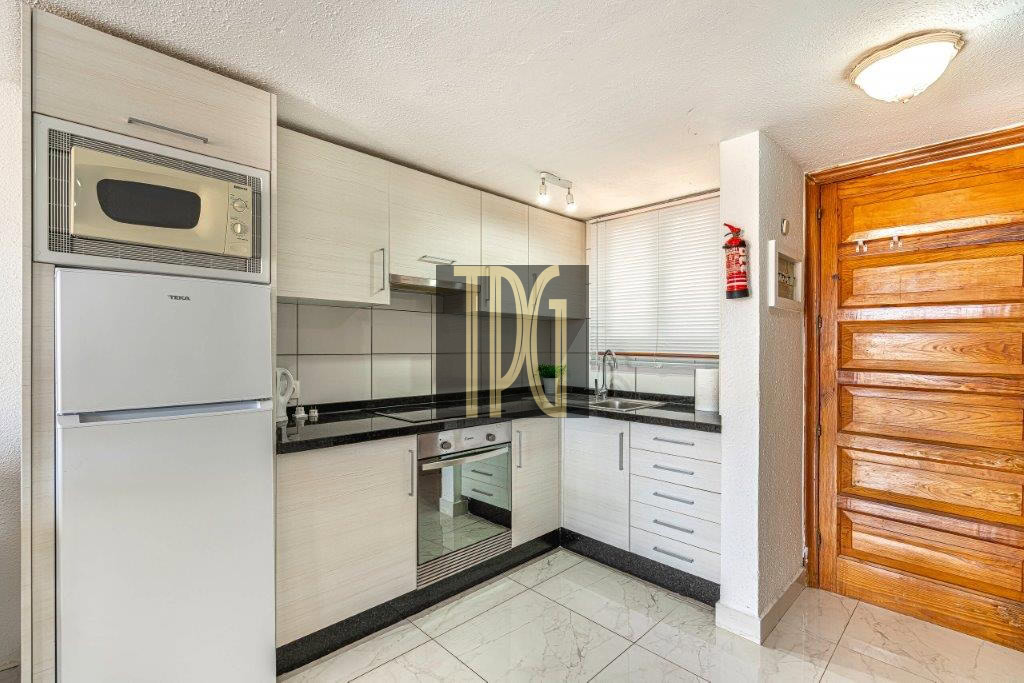 Modern L-shaped kitchen with white cabinets, black countertops, and built-in oven/microwave; wooden entry door on the right.