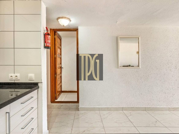 Bright kitchen with white cabinets and a black countertop, a wooden door center, and a red fire extinguisher on the left wall.