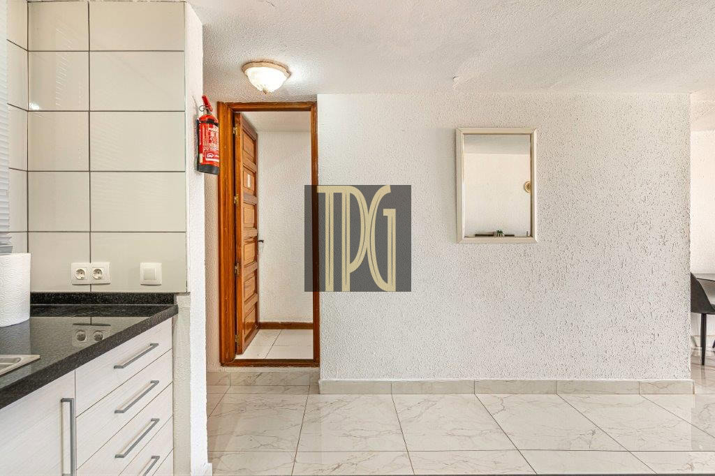 Bright kitchen with white cabinets and a black countertop, a wooden door center, and a red fire extinguisher on the left wall.