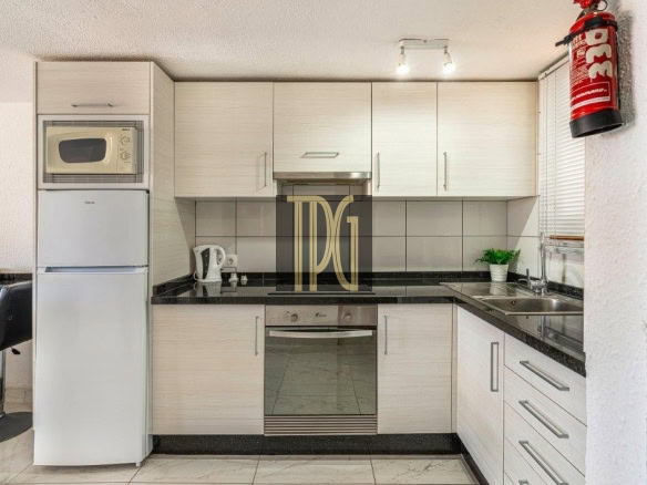 Modern white kitchen with black granite countertops, built-in oven, microwave, and a tall fridge on the left side.