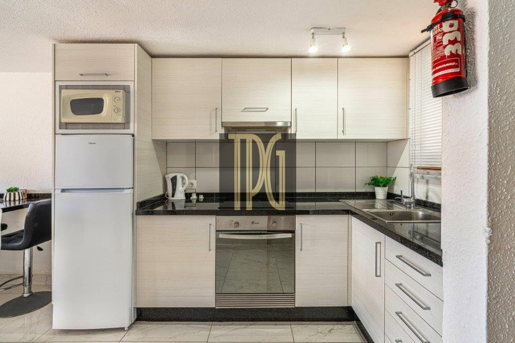 Modern white kitchen with black granite countertops, built-in oven, microwave, and a tall fridge on the left side.