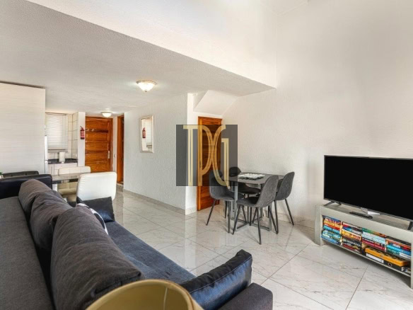 Open-plan living room with a dark gray sectional facing a flat-screen TV on a low stand and a compact bookshelf below.