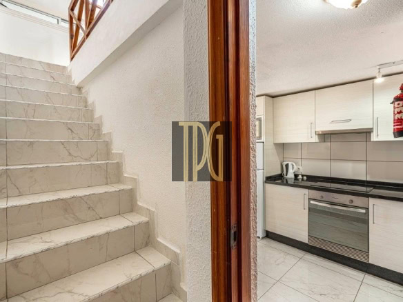 Interior view: marble staircase on the left and a compact white kitchen with stove and oven on the right, plus a red fire extinguisher mounted on the wall.