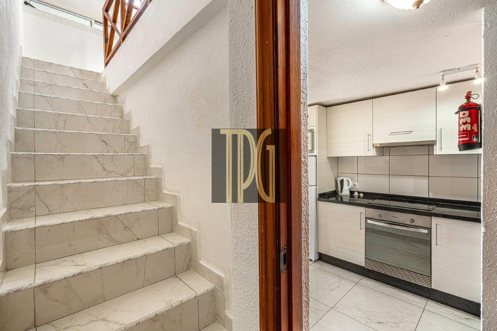 Interior view: marble staircase on the left and a compact white kitchen with stove and oven on the right, plus a red fire extinguisher mounted on the wall.
