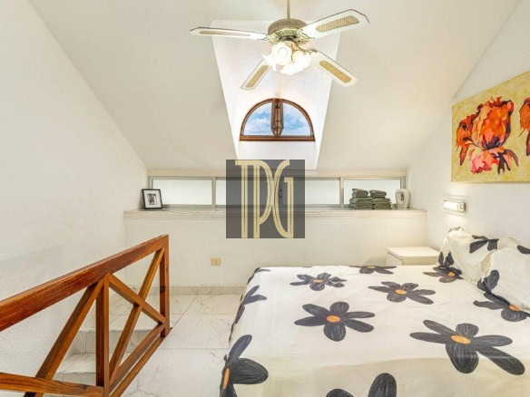 Cozy attic bedroom with a skylight, ceiling fan, and a bed covered in large black flowers on white bedding.