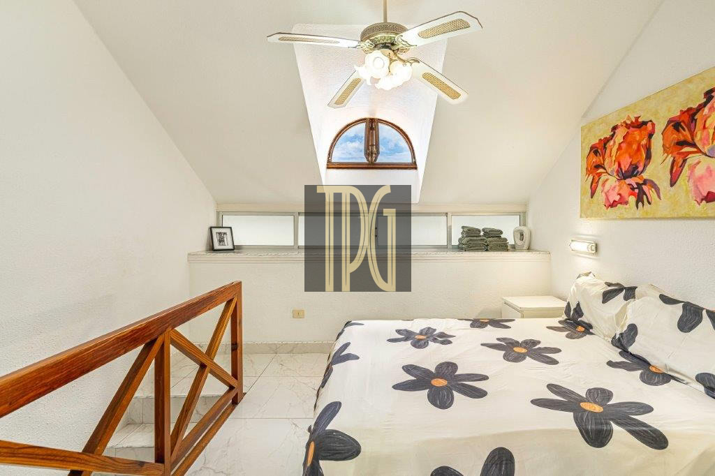 Cozy attic bedroom with a skylight, ceiling fan, and a bed covered in large black flowers on white bedding.