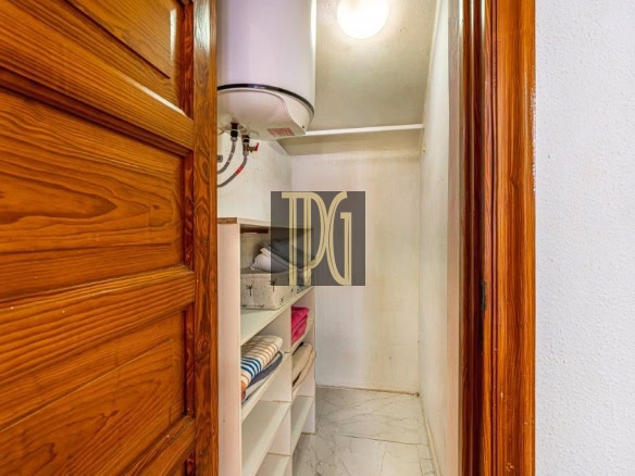 Small storage closet with white shelves holding folded towels and a ceiling-mounted water heater above the shelves in a narrow hallway closet.