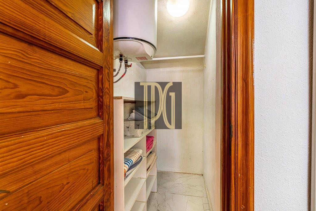 Small storage closet with white shelves holding folded towels and a ceiling-mounted water heater above the shelves in a narrow hallway closet.