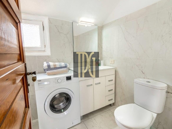 Small bathroom with a front-loading washing machine under a stack of towels, white vanity, and toilet.
