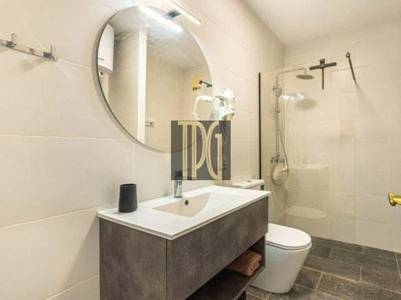 Modern bathroom with a round mirror above a white sink and dark vanity, glass shower enclosure, and toilet.