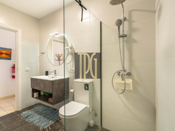 Modern bathroom with a glass shower enclosure, wall-mounted sink, and toilet; blue rug on a dark floor.