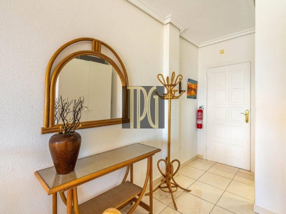 Entry hallway with a wooden console table, arched mirror, and vase of branches against a textured wall.
