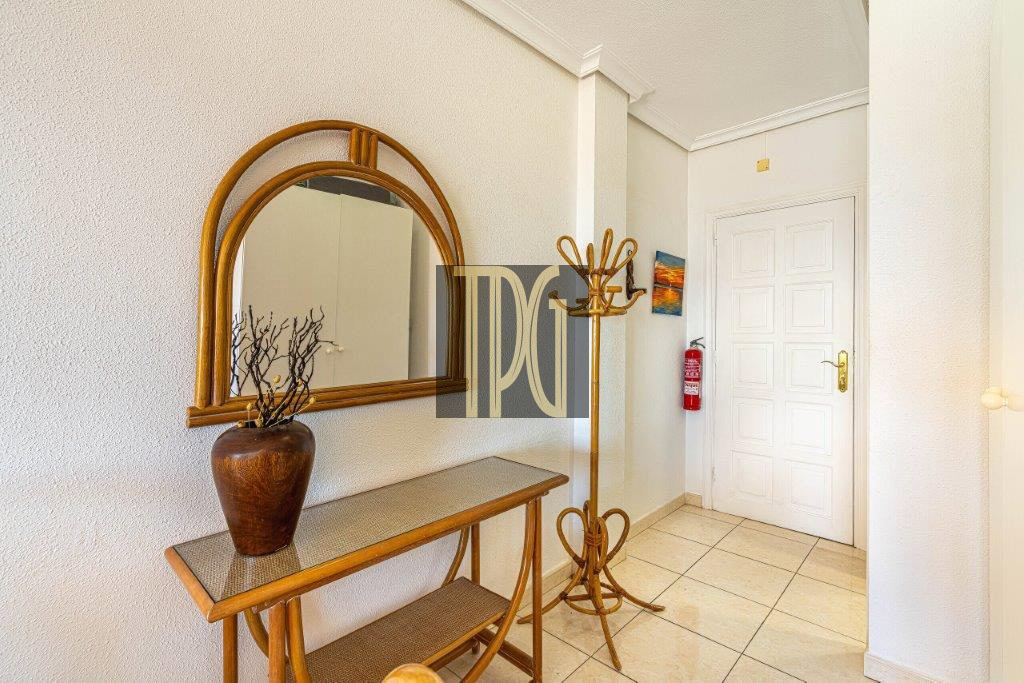Entry hallway with a wooden console table, arched mirror, and vase of branches against a textured wall.