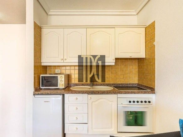 Compact kitchen with white cabinets, brown tile backsplash, and granite countertop featuring a microwave, sink, fridge, and oven-stove combo.