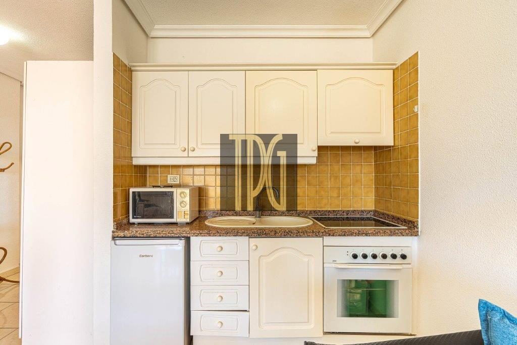 Compact kitchen with white cabinets, brown tile backsplash, and granite countertop featuring a microwave, sink, fridge, and oven-stove combo.
