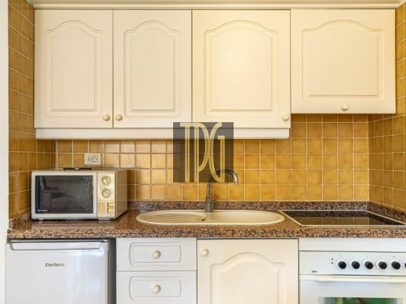 Compact kitchen with cream cabinets, brown tile backsplash, granite countertop, sink, stove, oven, microwave, and mini fridge.
