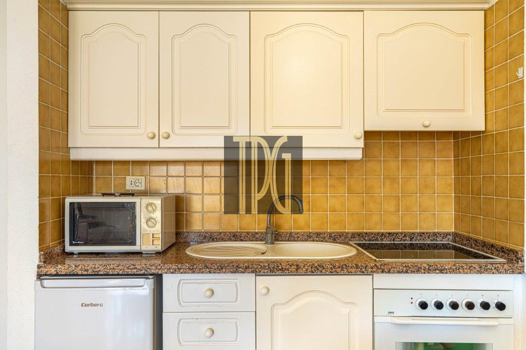 Compact kitchen with cream cabinets, brown tile backsplash, granite countertop, sink, stove, oven, microwave, and mini fridge.