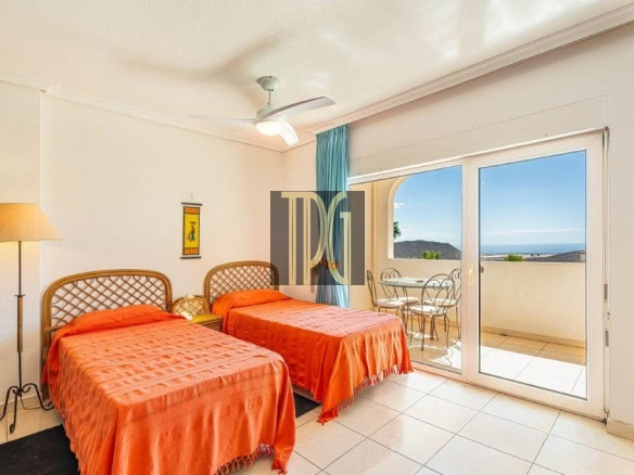 Twin bedroom with orange bedspreads, wicker headboards, a floor lamp, and sliding doors to a balcony with an ocean view.