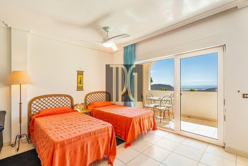 Twin bedroom with orange bedspreads, wicker headboards, a floor lamp, and sliding doors to a balcony with an ocean view.