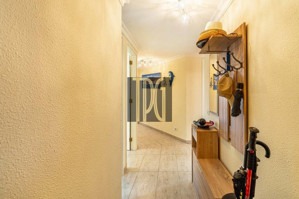 Bright yellow hallway with a wooden coat rack, hanging hats, and a small bench along the wall; doorway in the distance.