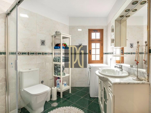 Bright bathroom with a glass shower enclosure, white toilet, and marble countertop sink by a wooden window.