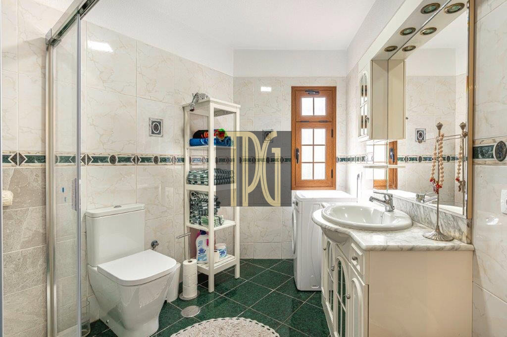 Bright bathroom with a glass shower enclosure, white toilet, and marble countertop sink by a wooden window.