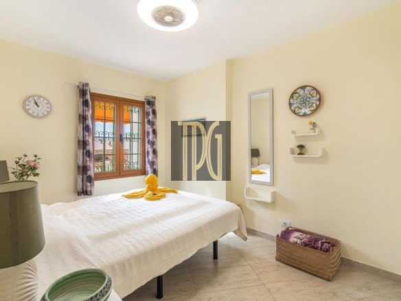 Bright bedroom with a white quilted bed, a yellow duck toy on the duvet, a window with patterned curtains, and a tall mirror on the right wall.
