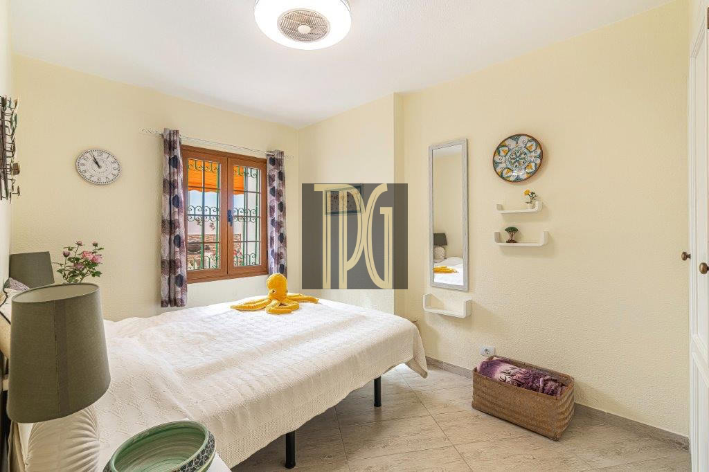 Bright bedroom with a white quilted bed, a yellow duck toy on the duvet, a window with patterned curtains, and a tall mirror on the right wall.