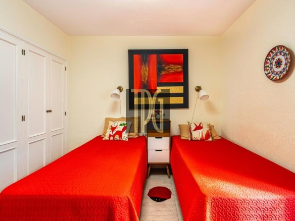Twin bedroom with two single beds in red quilts, white nightstand between, and wall art above; built-in white wardrobes along the left wall.