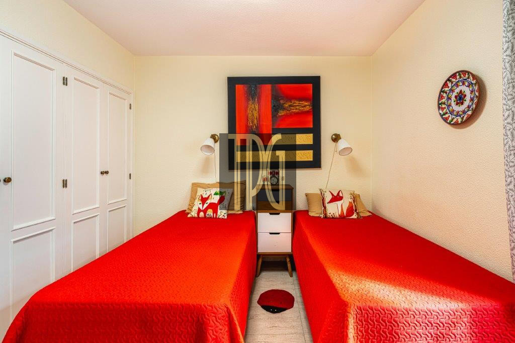 Twin bedroom with two single beds in red quilts, white nightstand between, and wall art above; built-in white wardrobes along the left wall.