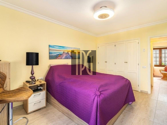Bright yellow bedroom with a purple bedspread, white built-in wardrobes, and a doorway to a sunlit seating area.