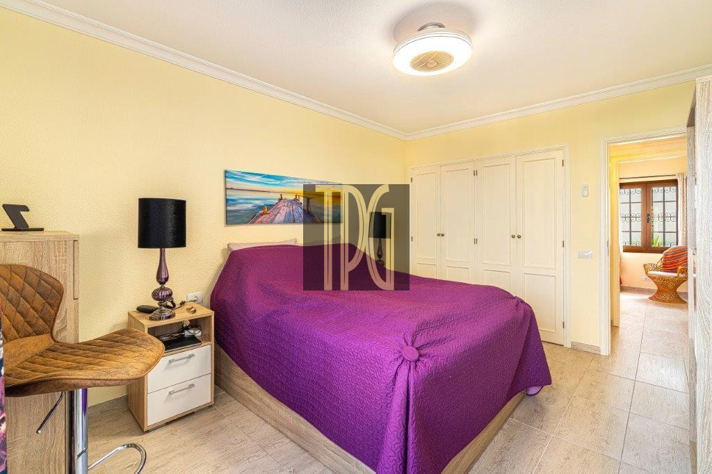 Bright yellow bedroom with a purple bedspread, white built-in wardrobes, and a doorway to a sunlit seating area.