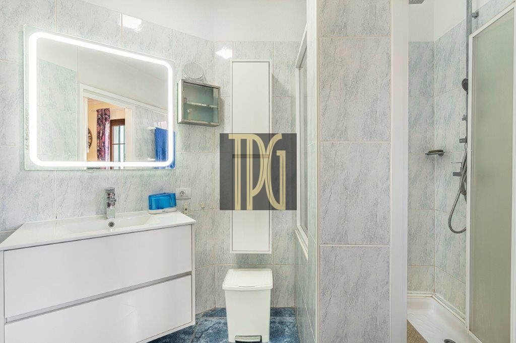 Bright modern bathroom with a backlit rectangular mirror above a white vanity and sink, blue accents, and a toilet nearby.