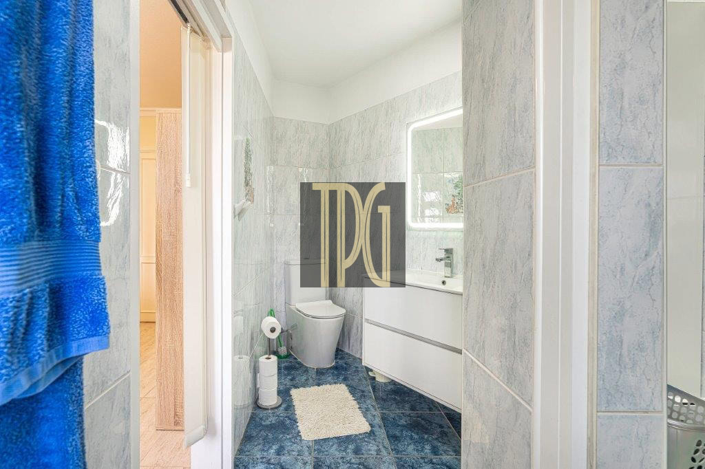 Small blue-tiled bathroom with a white vanity, toilet, and a fluffy rug on dark blue floor tiles, blue towels on the left.