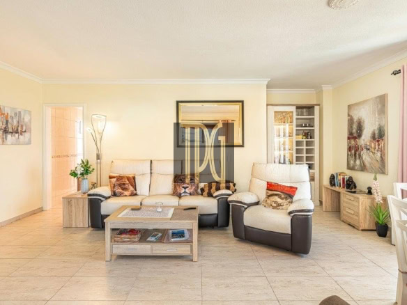 Bright living room with beige sofa set, two reclining chairs, and a wooden coffee table on light tile flooring across from a wall mirror.