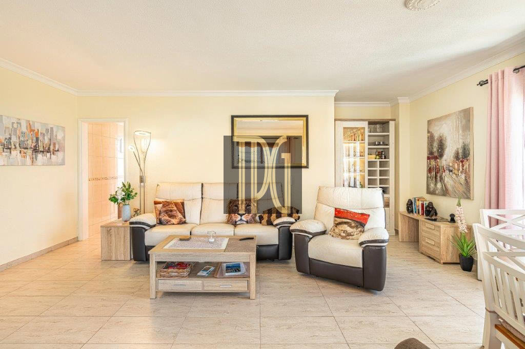 Bright living room with beige sofa set, two reclining chairs, and a wooden coffee table on light tile flooring across from a wall mirror.