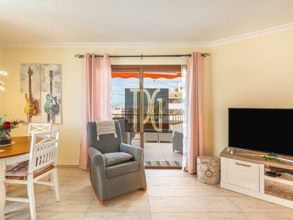 Cozy living room with a gray armchair facing a TV, sliding glass door to a balcony, and pastel pink curtains