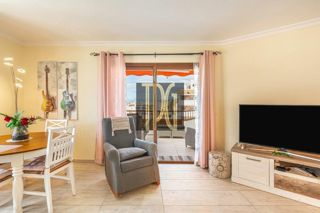 Cozy living room with a gray armchair facing a TV, sliding glass door to a balcony, and pastel pink curtains