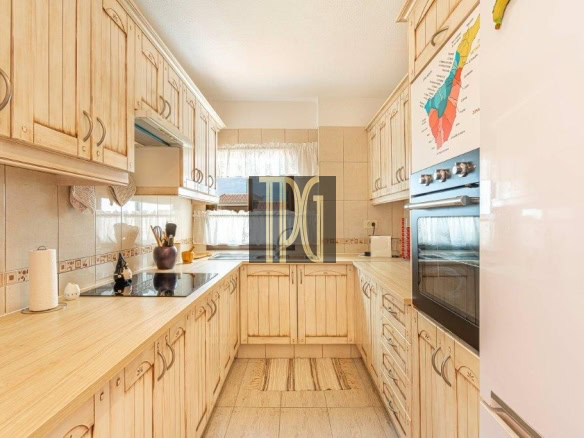 L-shaped kitchen with light wood cabinets, beige countertops, and built-in oven on the right wall.